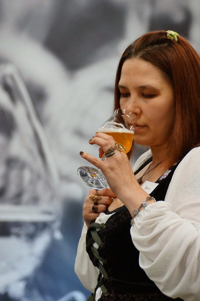 Me sniffing a glass with the StiBONfire rauchhelles in it. Pinkbrownish shoulderlength hair with a selfmade green crunchy with a hopplant print, white shirt with wide long sleeves and a corsetstyle waistcoat with dark green ribbons and brownish vine embroidery.
