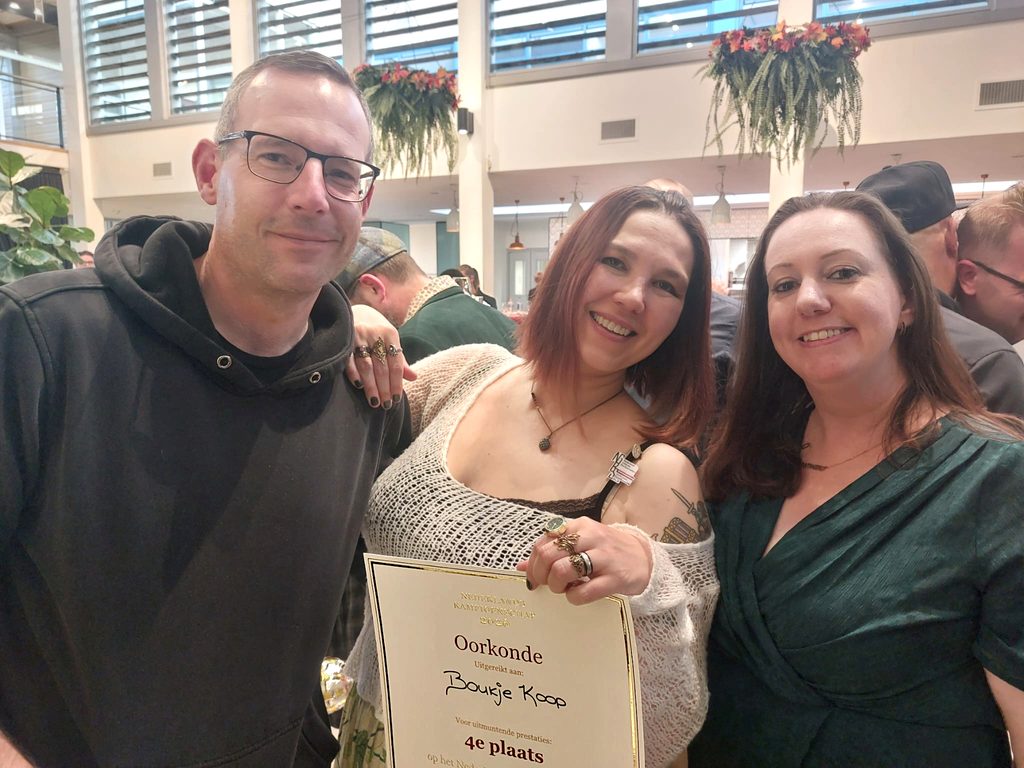 My husband Paul and metamour Anneke with me in the middle holding the certificate, all smiling widely towards the camera.